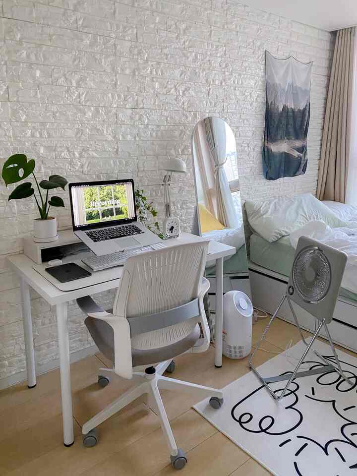 白いレンガ壁と木目調の床が調和する寝室、シンプルな白いデスクとチェア、全身鏡とベッドが配置された清潔感のあるワークスペース。
