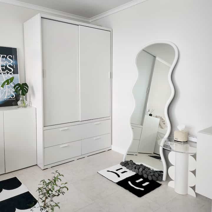 白を基調とした広々としたリビング、幅広いクローゼットと曲線的な全身鏡が配置されたシンプルなインテリア