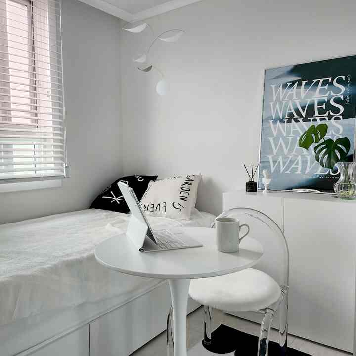 白を基調とした寝室、白いベッドとクッション、丸テーブルとアクリルチェアが配置されたシンプルでモダンなインテリア