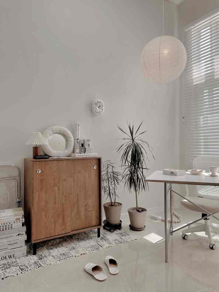 ナチュラルカラーとウッドトーンが調和したリビング、木製キャビネットと植物、ホワイトブラインドとオフィスチェアが配置されたシンプルで落ち着いたインテリア