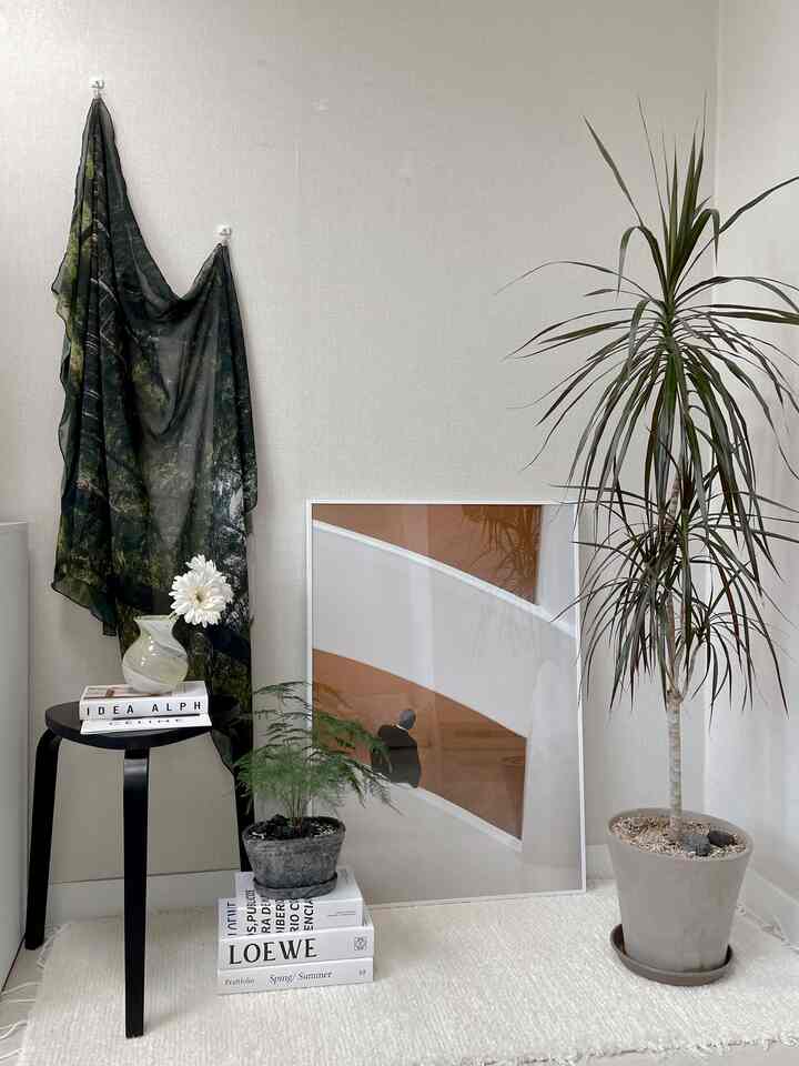 明るいベージュの壁と白いラグの上に黒いスツールと植物、ポスターが配置されたナチュラルなリビングのコーナー