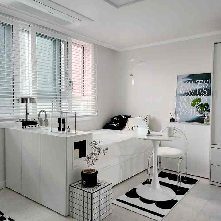 白とモノトーンの色調の一人用寝室、収納付きベッドと丸テーブル、アクリルチェアが配置された清潔でモダンなインテリア