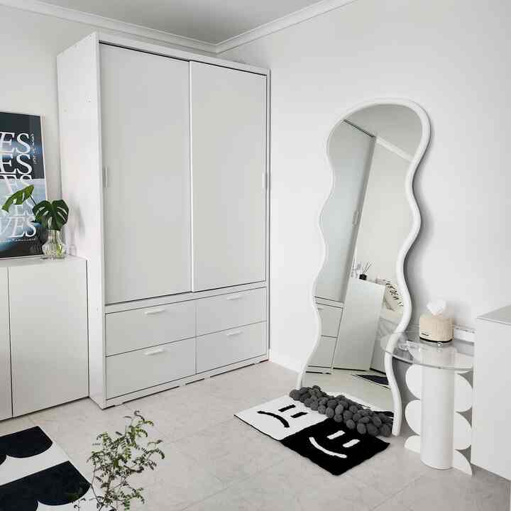 白を基調とした寝室、大きなスライド式クローゼットと独特な曲線の鏡が配置されたモダンで清潔感のあるインテリア