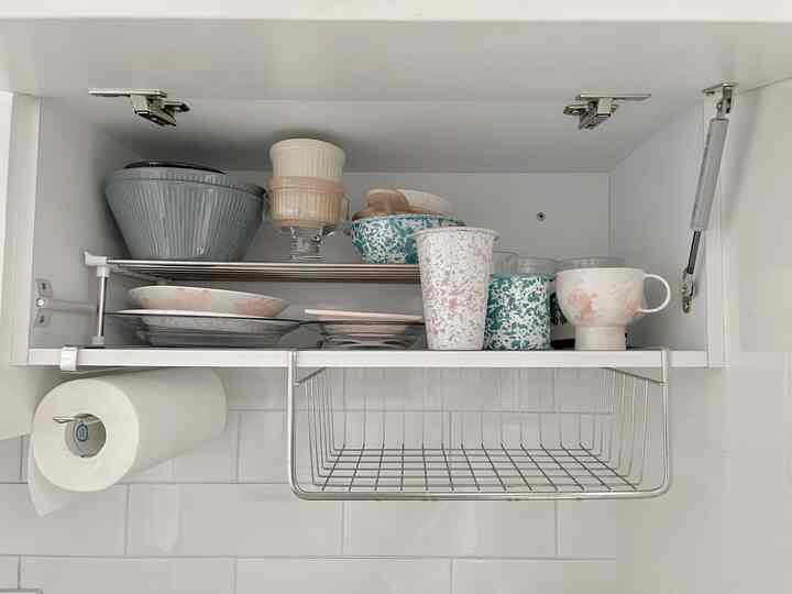 白を基調としたキッチンキャビネット内、整然と並べられたカラフルなボウルやマグカップ、タオルが配置された清潔感のある空間