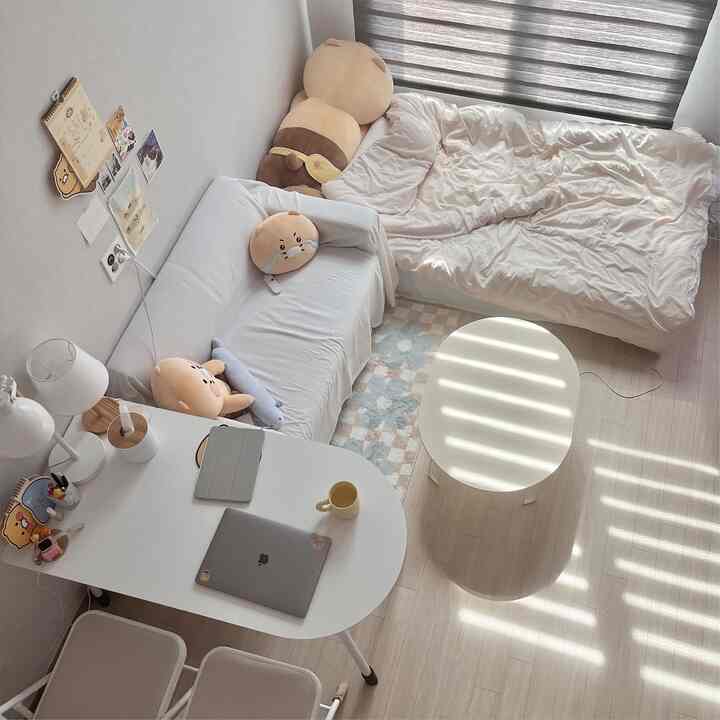 ホワイトとベージュのトーンの一人暮らしの部屋、安定感のあるレイアウトで壁に寄せられたソファとベッド