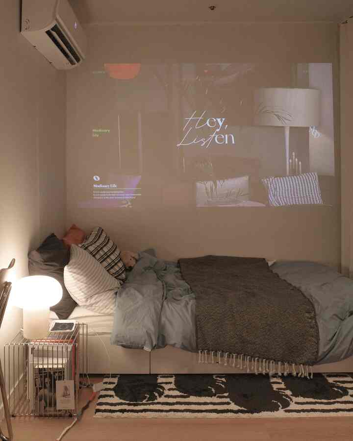 白い壁と茶色い床のスーパシングル寝室、低いマットレスと鮮明なプロジェクター画面が落ち着いた雰囲気のあるインテリア