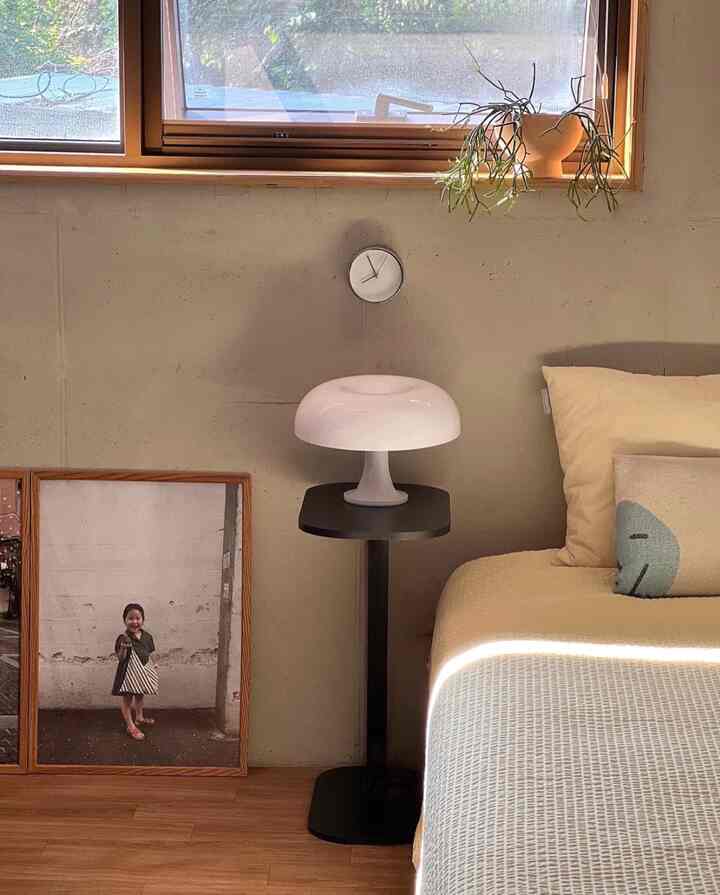 ベージュと木目調の寝室、白いテーブルランプと黒いサイドテーブル、ベッドカバーが配置された自然な雰囲気のインテリア