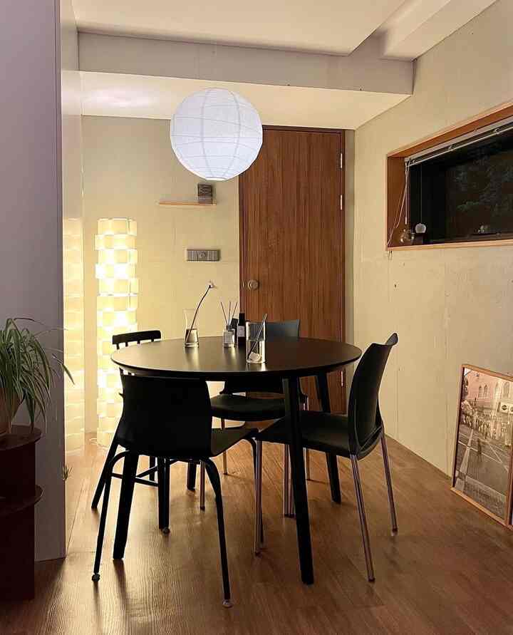 木目調の床と扉、黒い円形のダイニングテーブルと椅子が配置されたワンルームのダイニングスペース