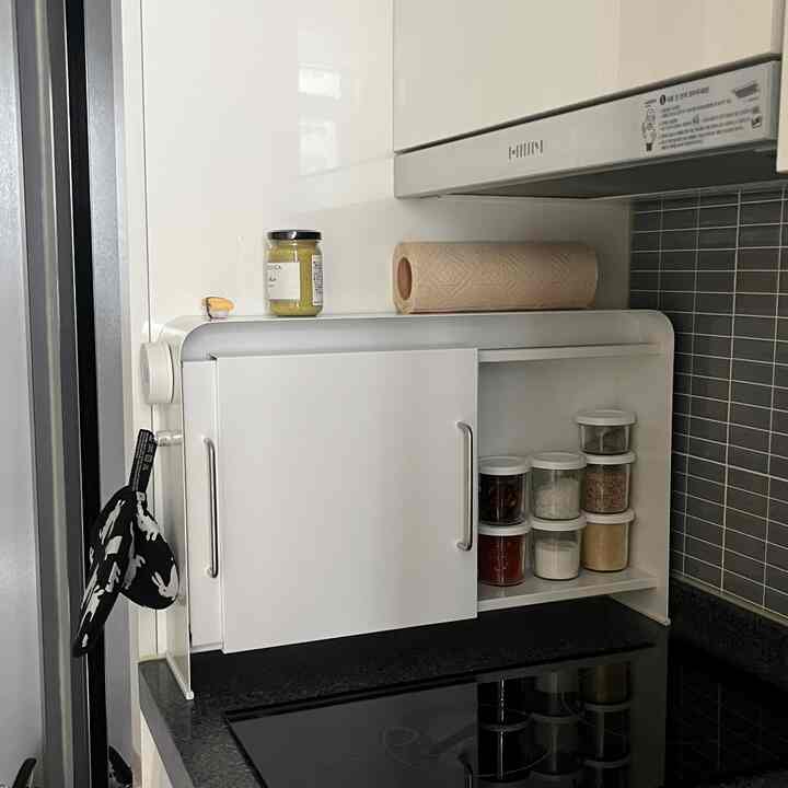 清潔感のある白を基調としたキッチン、スリムな鉄製収納キャビネットに調味料とキッチンタオルが整頓されたミニマルな空間