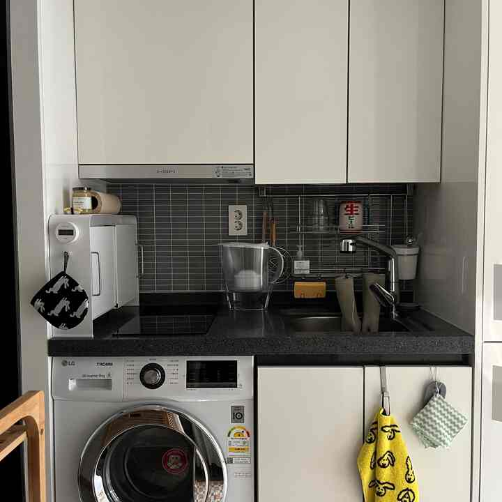 ホワイトとグレーのトーンのコンパクトなキッチン、洗濯機とシンクが配置された清潔で機能的なインテリア