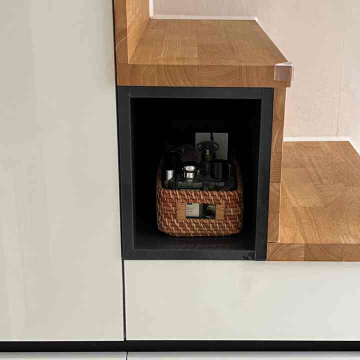 ナチュラルカラーのキッチン収納スペース、木製バスケットに香水と薬が整頓された印象的な空間