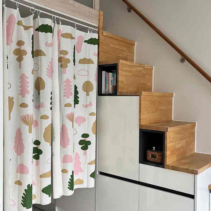 ナチュラルな色調のロフトオフィステルの階段スペース、収納された木製階段と模様入りカーテンが配置された雰囲気のある空間