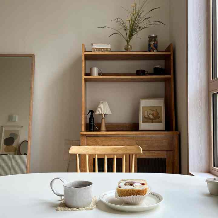 ベージュと木目調のリビング兼ダイニング空間、木製の椅子とテーブル、コーヒーカップとケーキが置かれた雰囲気のあるおうちカフェ