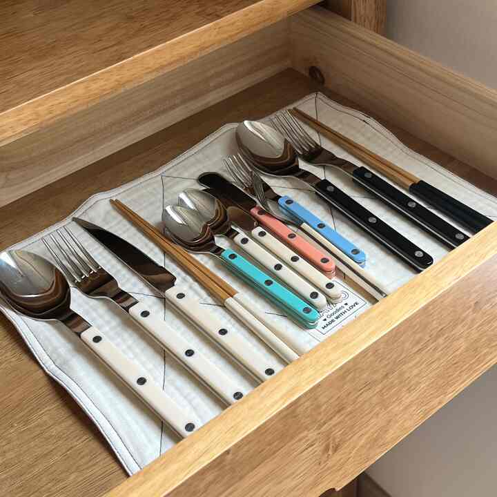 アイボリーとブラックの木製の引き出しに、色とりどりのカトラリーと箸が整然と収納されたキッチンスペース