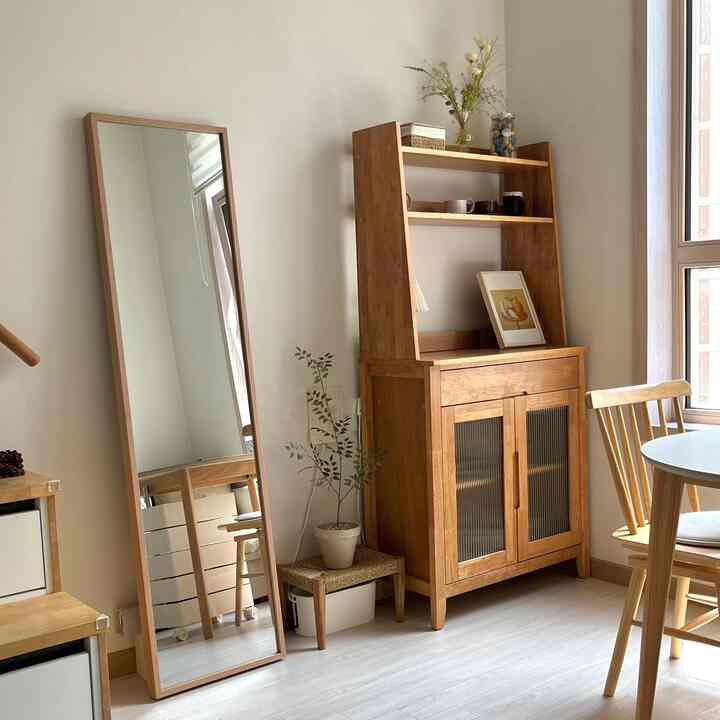 温かみのある木目調のリビング、木製の全身鏡とキャビネットが配置され、カフェ風の落ち着いた雰囲気のインテリア
