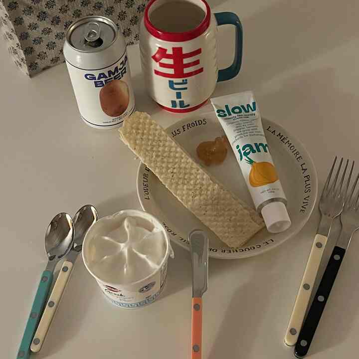 ホワイトとベージュの色調のテーブルトップにカトラリー、飲料缶、クリームアイスクリーム、皿が配置されたおうちカフェ風のデザートセッティング空間