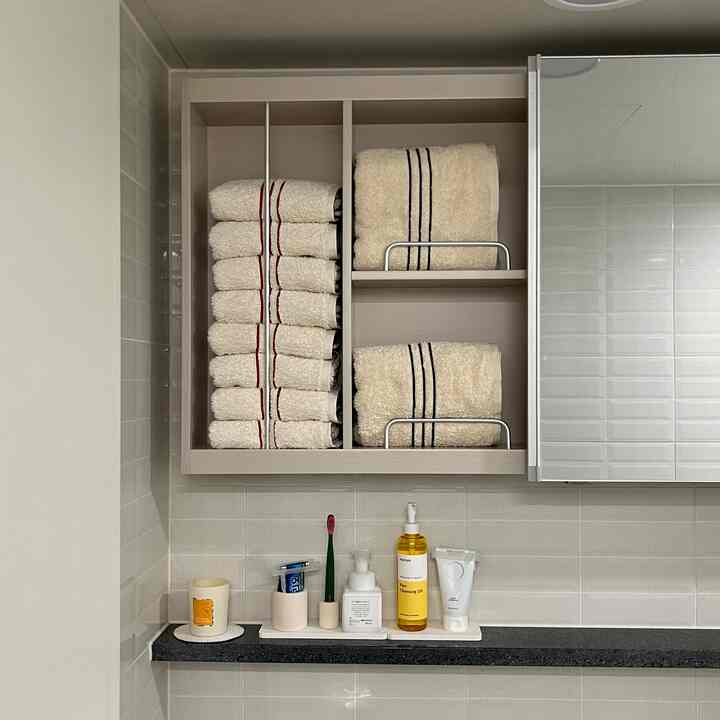 白とベージュのトーンのバスルーム、収納棚に珪藻土トレイとストライプのタオルが整然と置かれたミニマルな空間