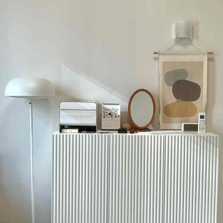 柔らかな白と木目調のポスターが調和するワンルームリビング、シンプルな収納キャビネットが配置された印象的な空間