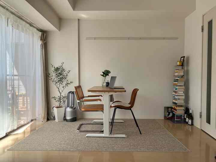 ホワイトとベージュのトーンのナチュラルモダンなホームオフィス、木製デスクとラタンチェア、ベージュのラグが落ち着いた雰囲気を演出