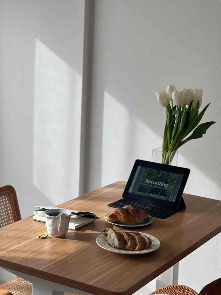 白い壁と木目調のダイニングテーブルがあるナチュラルモダンなホームカフェ、チューリップとデジタル機器が配置された雰囲気のあるインテリア