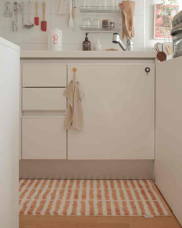 明るいアイボリー調のキッチン空間、オレンジと白のストライプ柄ラグが敷かれた自然で温かみのある雰囲気のインテリア