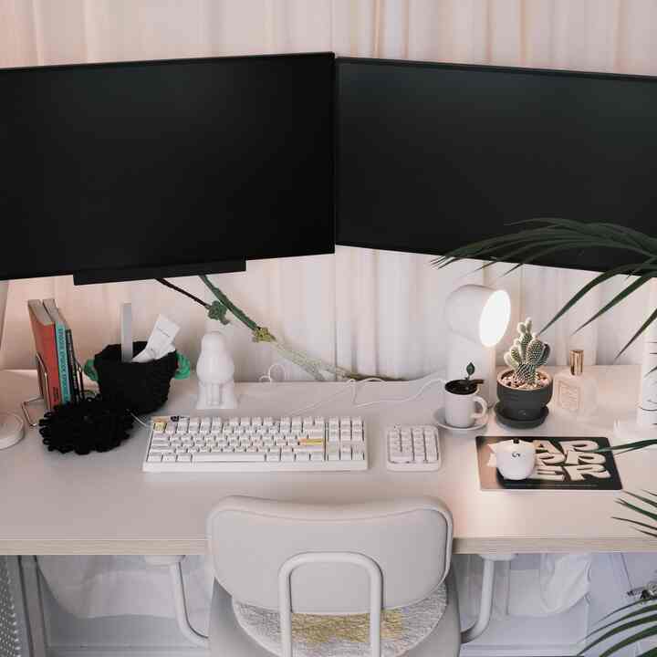 白を基調としたホームオフィス、デュアルモニターとシンプルなデスク、チェアが配置された清潔感のある作業空間