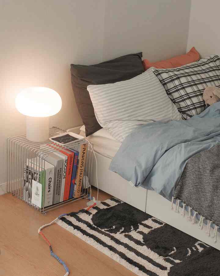 白と茶色のトーンの寝室、白いベッドに多様な枕、テーブルランプとラグが居心地の良い雰囲気を作る空間