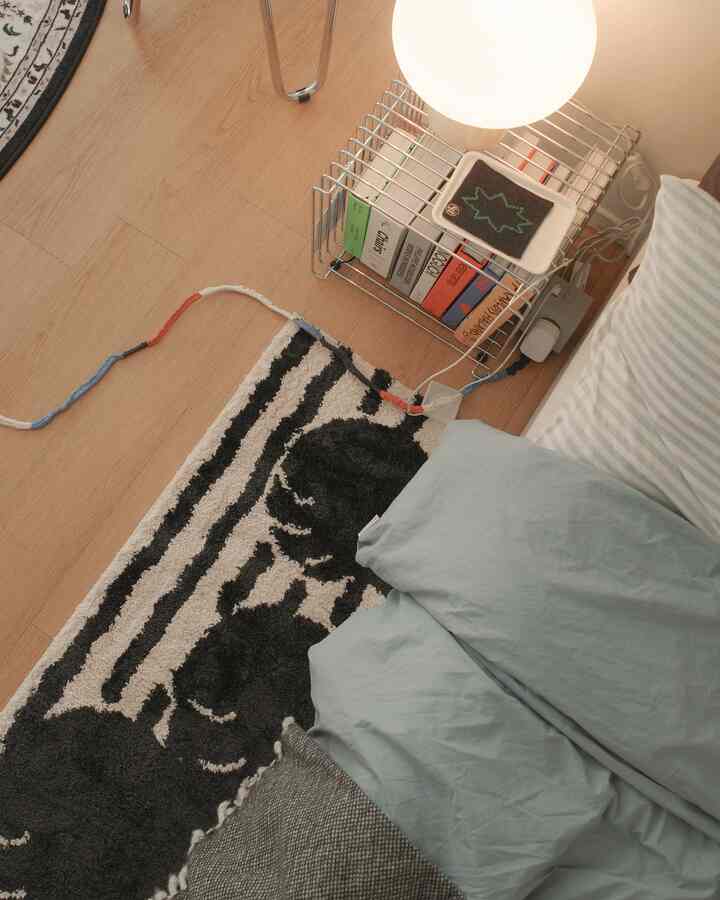 ナチュラルカラーの寝室、猫柄のラグとベッド、テーブルランプが配置された温かみのある空間