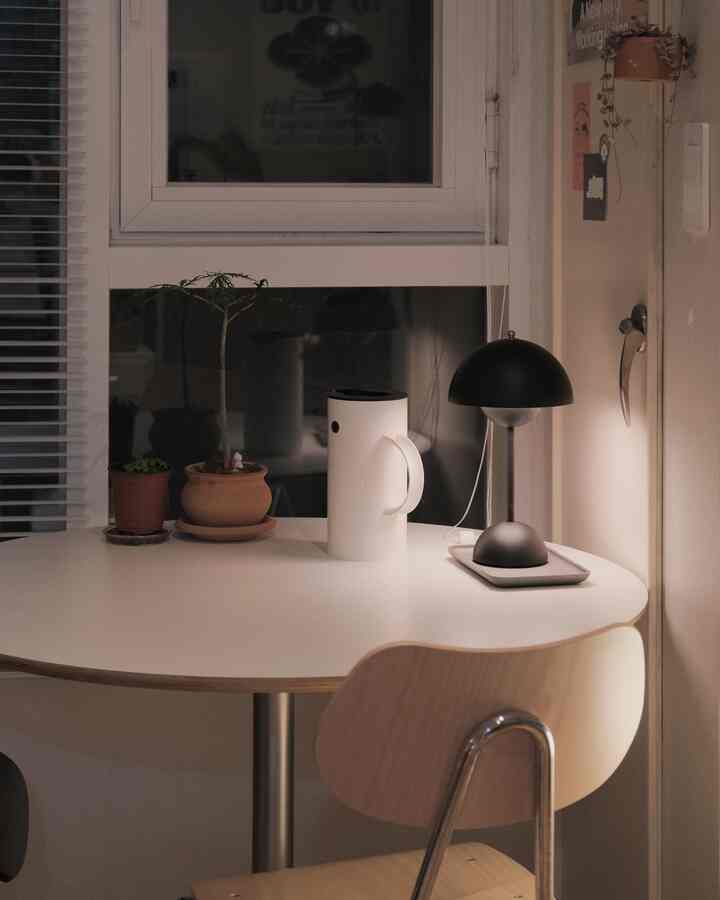 柔らかいホワイトとシルバートーンのダイニングルーム、丸テーブルの上にテーブルランプと植物が置かれ、落ち着いた雰囲気のインテリア