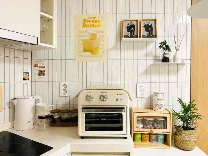 白いタイル壁と木製シェルフが配置されたシンプルでナチュラルなキッチン、中央にクリーム色のエアフライヤーオーブンと電気ケトルが置かれている