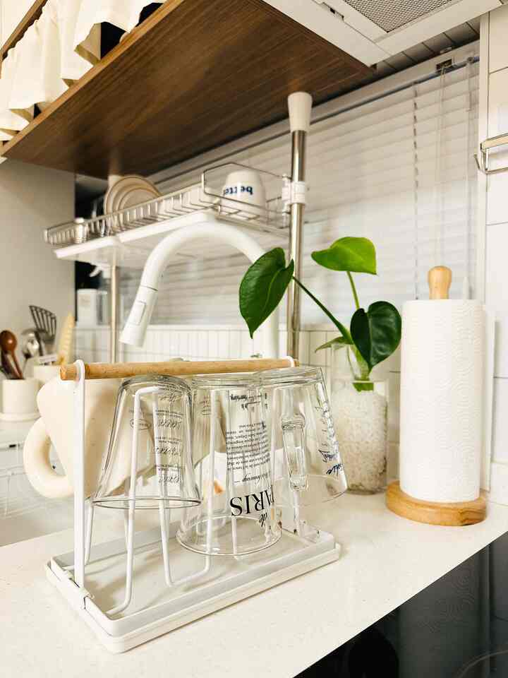 白と木目調が調和したキッチン、カップ乾燥ラックにガラスとマグカップが整頓された雰囲気のあるインテリア