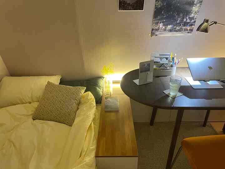 暖かいベージュとナチュラルカラーのトーンの寝室、左にベッドとナイトテーブル、右に木製のデスクが配置された居心地の良い空間