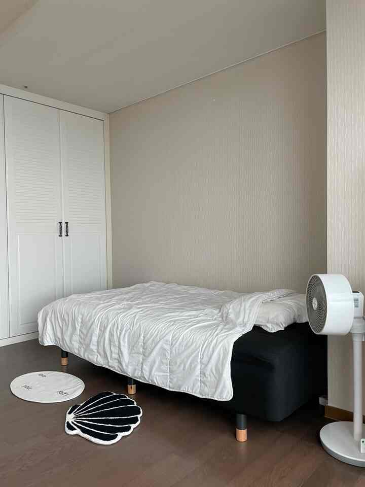 ホワイトとブラックの色調の寝室、シンプルなベッドと清潔な壁、扇風機と小さなラグが配置された落ち着いた空間