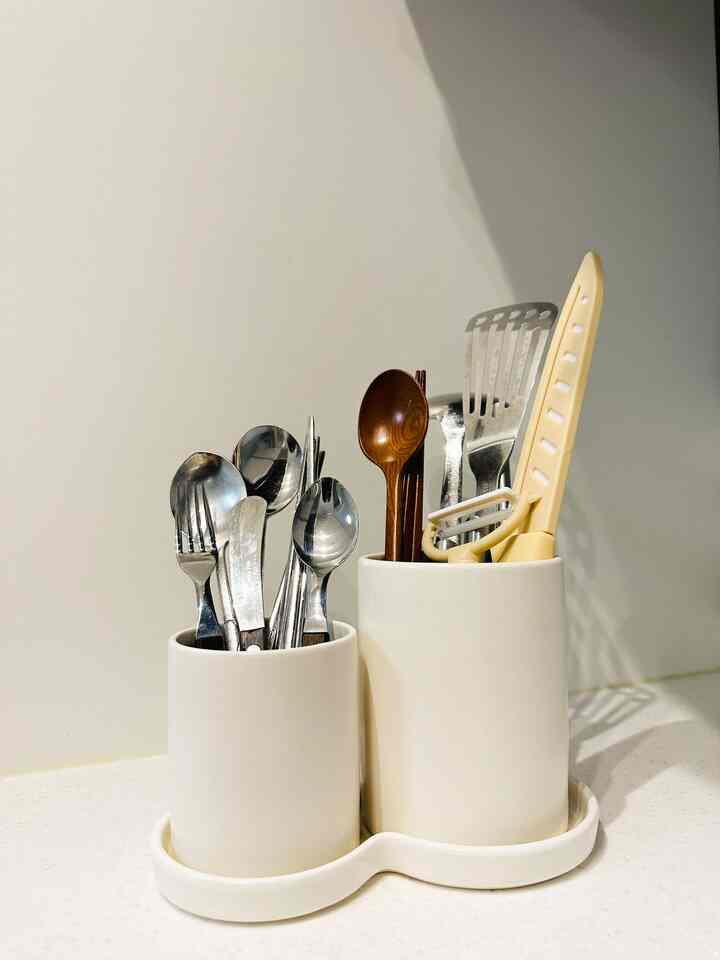 白を基調としたキッチン、カトラリーホルダーに食器類や調理器具が整然と配置された雰囲気のあるインテリア