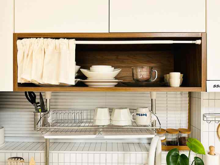 白と木目調が調和したキッチン、皿やボウルが整然と並べられた棚とシンク上の棚がある雰囲気のあるインテリア