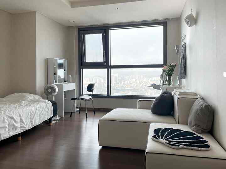 白とベージュの色調のワンルーム、シングルベッドとソファ、デスクが配置されたシンプルでモダンな印象的な空間