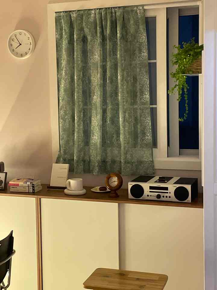 緑の植物柄カーテンと白い木目調収納棚が配置された温かみのある空間