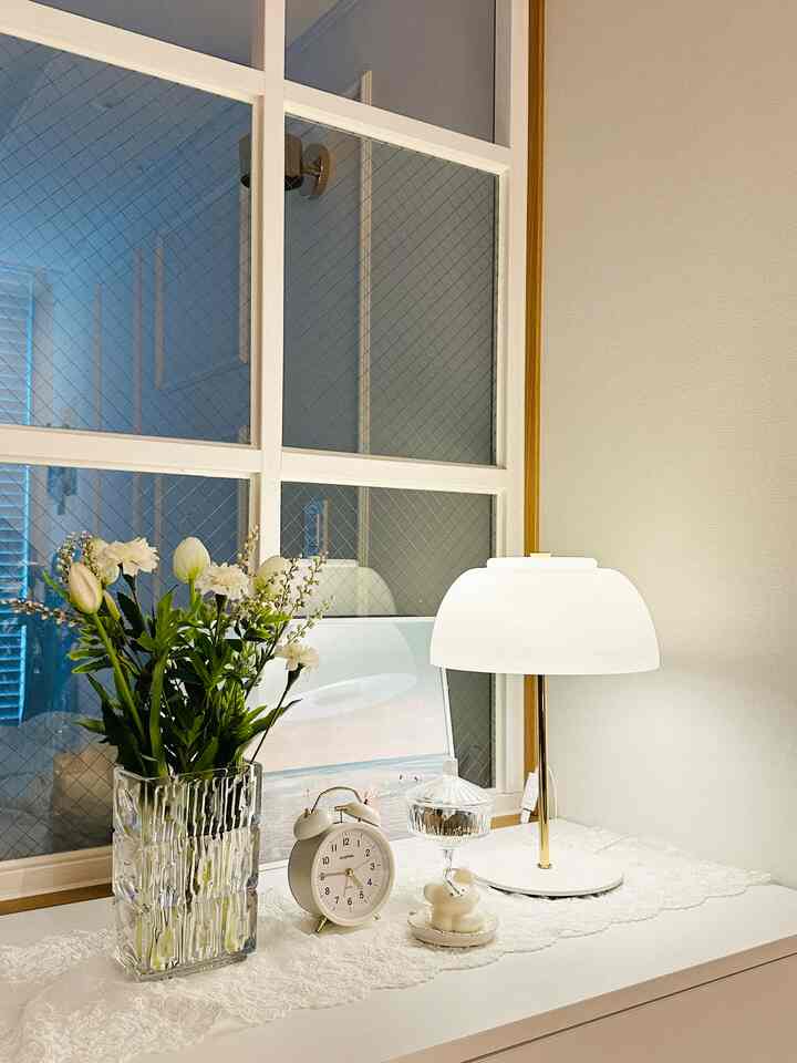 白とゴールドの色調の玄関収納の上に額縁、テーブルランプ、花瓶が配置された清潔感のある空間