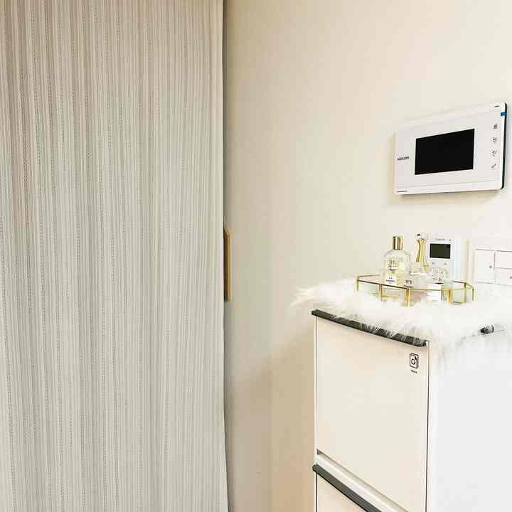 白とベージュのトーンの玄関、カーテンと整頓されたシューズラックが配置された落ち着いたモダンな空間