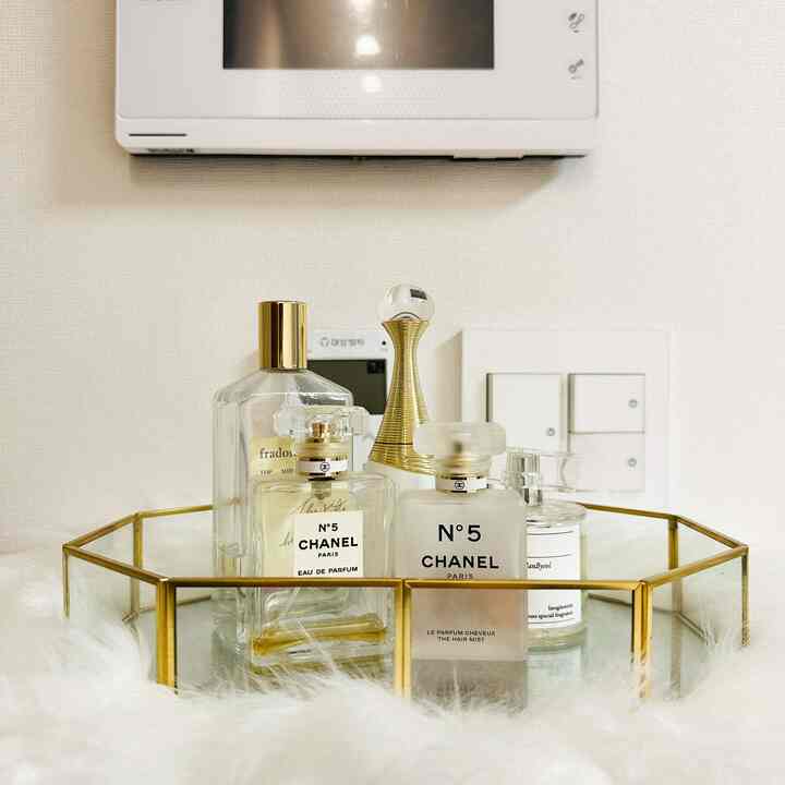 白い壁と金色のフレームトレイに置かれた香水瓶が配された、すっきりとした玄関の小物空間