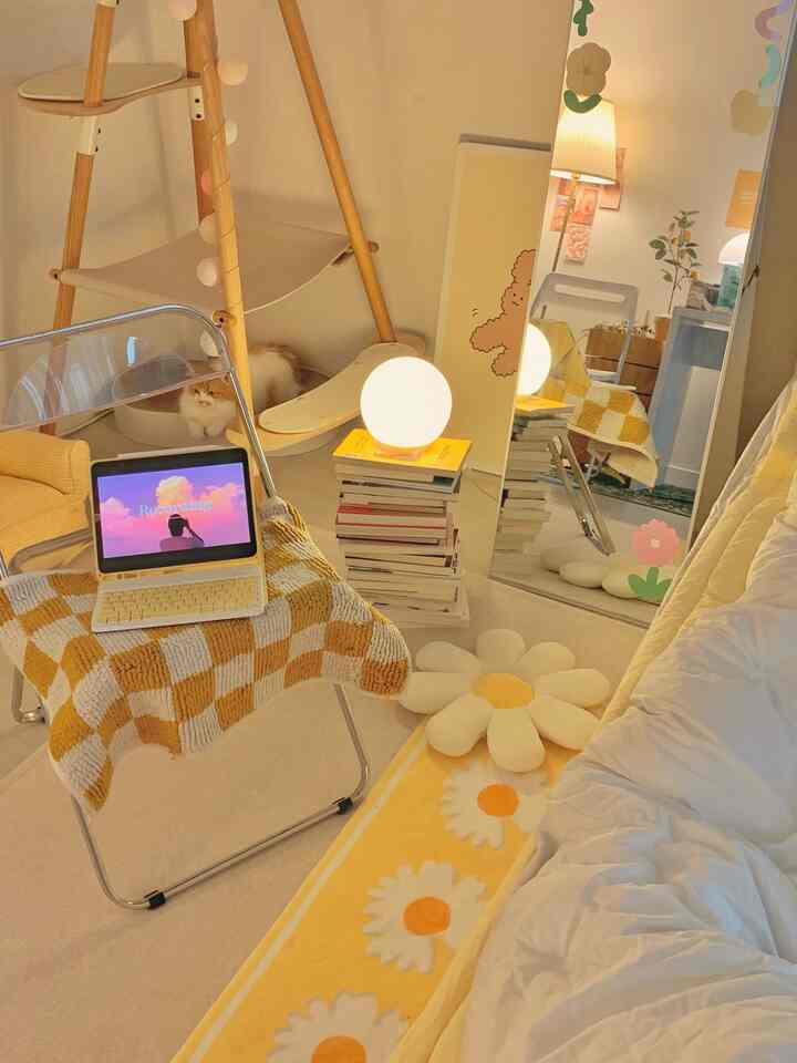 暖かい黄色とベージュのトーンの寝室、チェック柄のブランケットがかかる透明な椅子と猫がいる木製キャットタワーが配置された居心地の良い空間