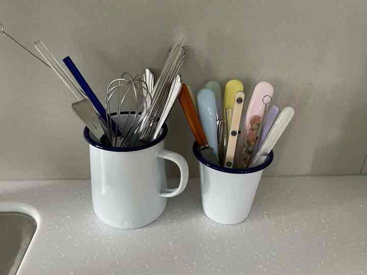 白と青のトーンのキッチンカウンターに並んだ2つのエナメルジャグがカトラリーを収納した清潔感のあるキッチン小物のインテリア