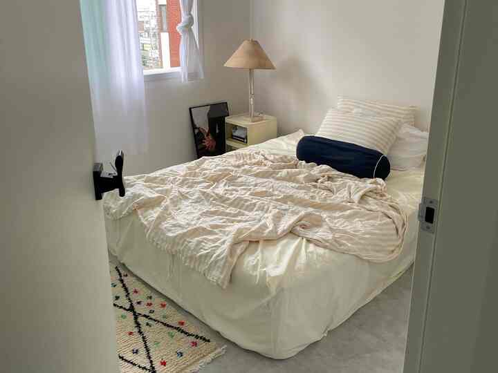 白とアイボリーの落ち着いた色調のシンプルな寝室、中央にベッドとナイトテーブル、パターンのラグが配置された雰囲気のあるインテリア