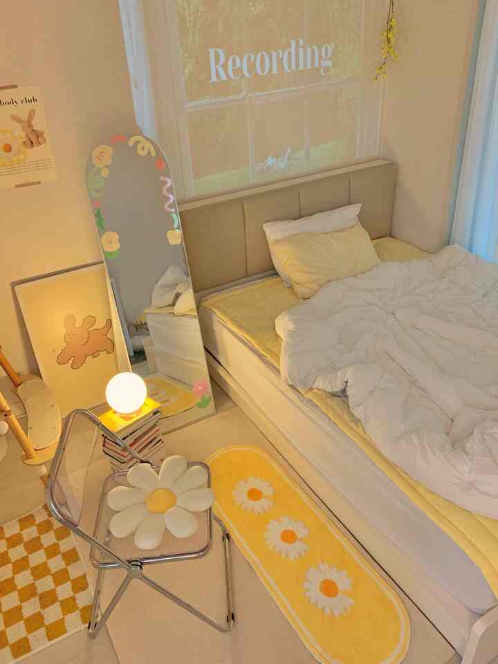 バター色と白色のトーンでまとめられた寝室、枕と寝具が配置されたベッドと透明な折りたたみ椅子がある雰囲気のある空間