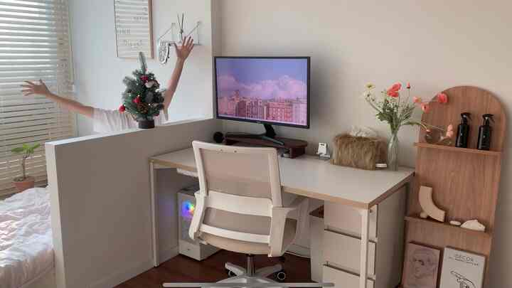 白と木目調のワンルームホームオフィス、デスクとコンピューター、クリスマスミニツリーが配置された雰囲気のある空間