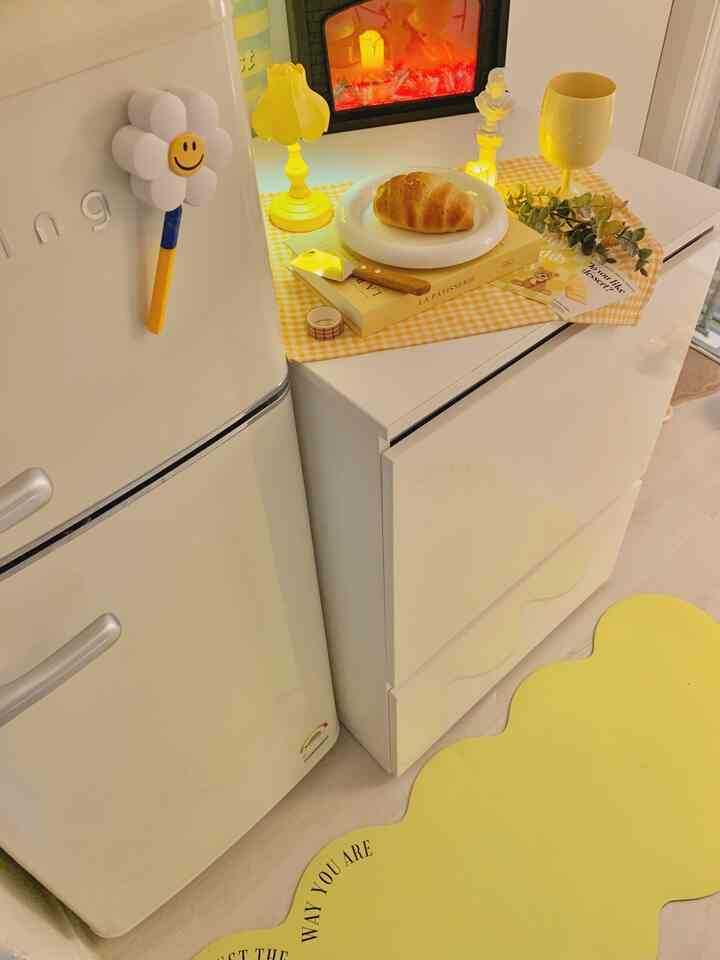 黄色と白のトーンのワンルームキッチンスペース、レトロなミニ冷蔵庫と黄色いテーブルランプが温かみのある雰囲気を演出