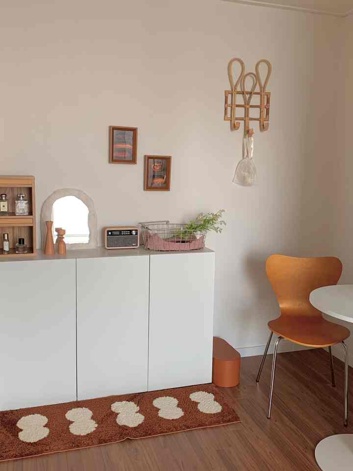 白い壁と木目の床、ラタンのハンガーと木製の椅子があるカフェ風の空間