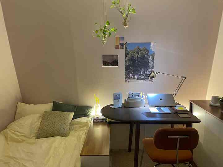 白い壁とブラウンの床が特徴のコンパクトな一人暮らしの寝室、デスクとオフィスチェアが配置された居心地の良いホームオフィス空間