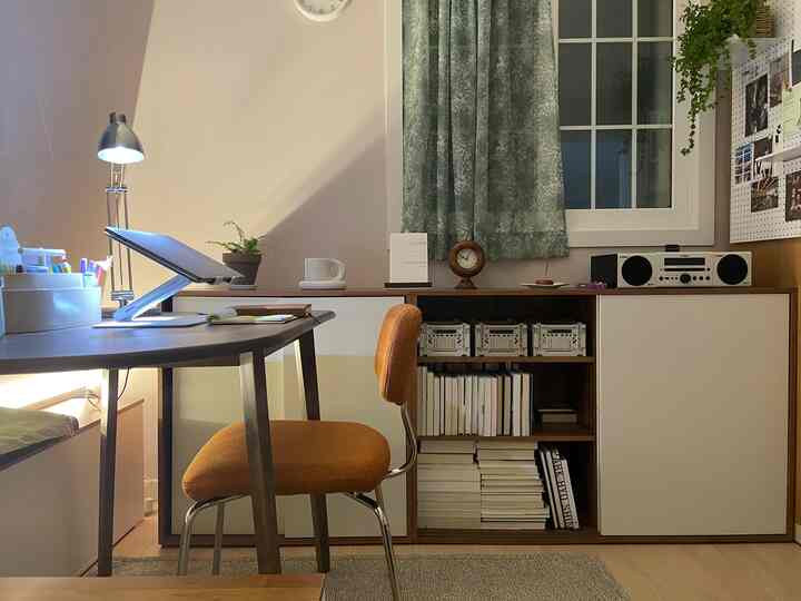 ベージュの壁のホームオフィス、チャコールのデスクとオレンジ色の椅子、木目調の収納キャビネットが配された雰囲気のあるインテリア