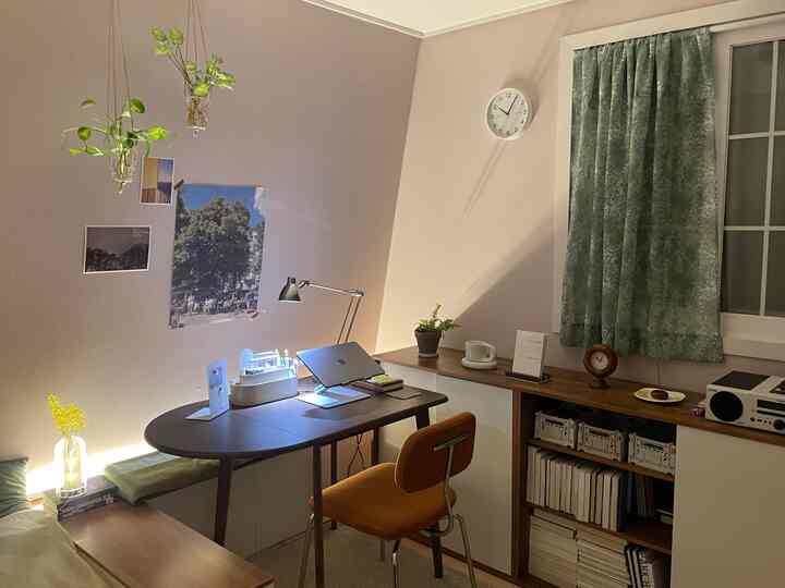 ベージュとブラウン調のホームオフィス、ダークブラウンのデスクとオレンジの椅子、緑の植物が配置された落ち着いた雰囲気の空間